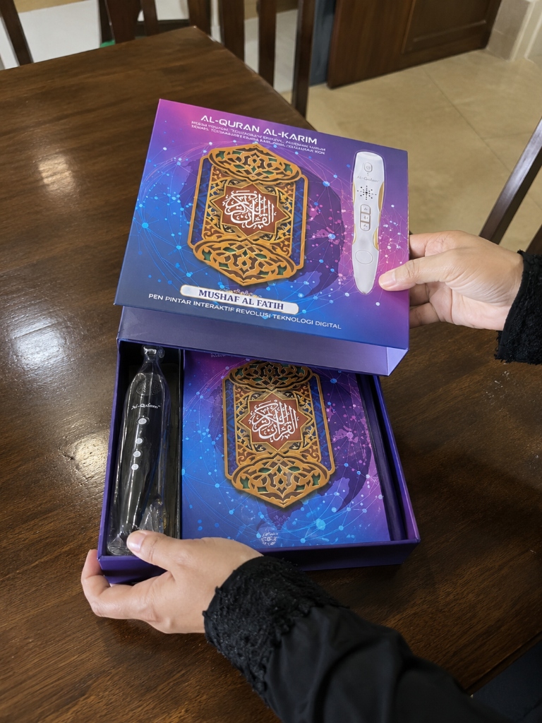 Gambar snap fon pelanggan: Tangan unbox kotak ungu Mushaf Al-Fatih nampak pen & Quran