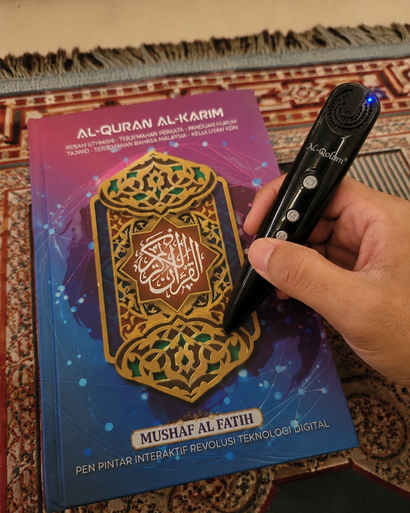 Gambar snap fon pelanggan: Pegang pen Al-Qolam hitam dengan Quran tertutup atas sejadah